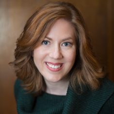 Margot Bloomstein, smiling with red hair and green sweater on brown background