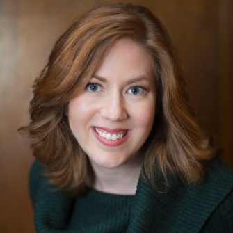 Margot Bloomstein, smiling with red hair and green sweater on brown background