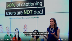 A woman in a blue dress standing in front of a slide saying: "80% of captioning users are NOT deaf" with text in front of her saying: "or when content is complicated or difficult to understand"