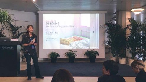 Carina speaking on stage in front of first presentation slide.