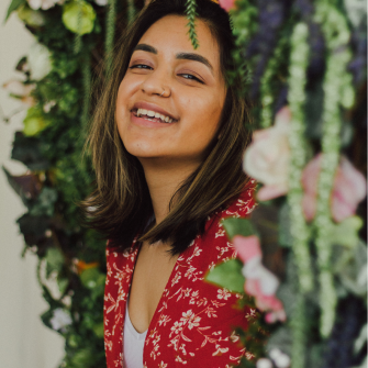 Headshot of Aleenah in a red dress with florals in the background