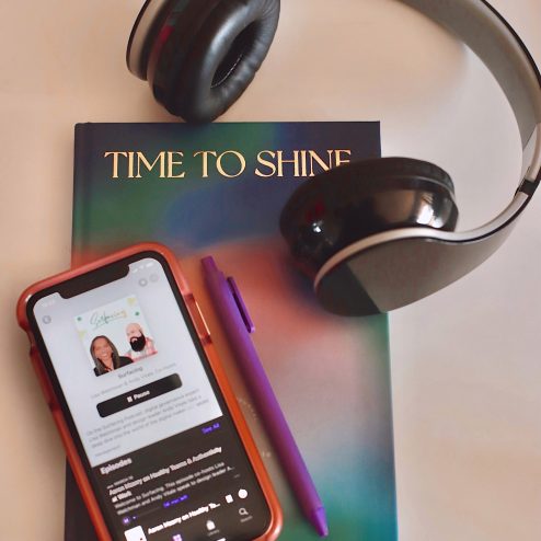 notebook with a phone sitting on it open to the podcast app with headphones next to the phone